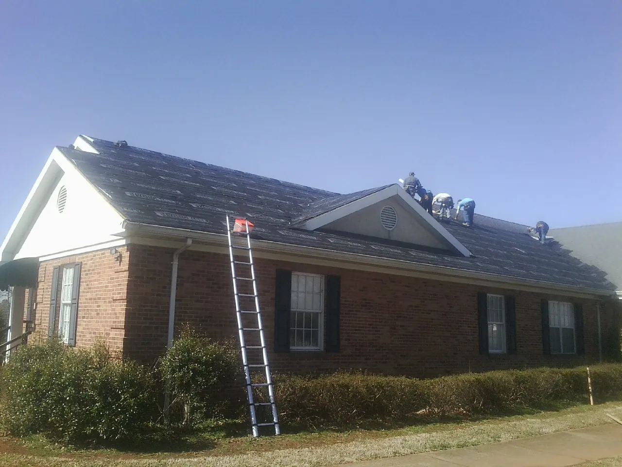 Crew tearing shingles off a brick ranch roof with a ladder set — Metal Roof Repair work by our crew in Pompton Plains