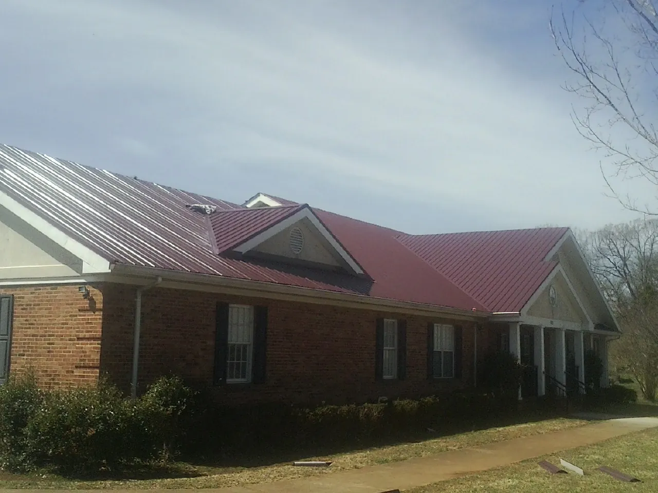 Red metal roof with gabled entries on a long brick building, from a Hail Damage Roof Repair job in Pompton Plains