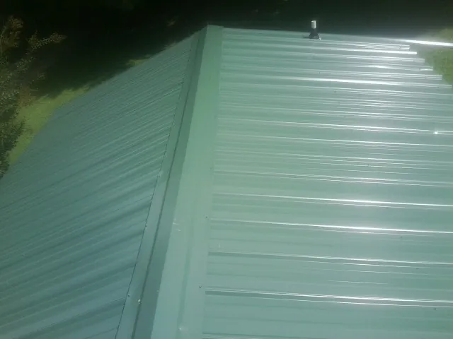 New green metal panels meeting at the ridge of a roof — Flat Roof Repair work by our crew in Pompton Plains