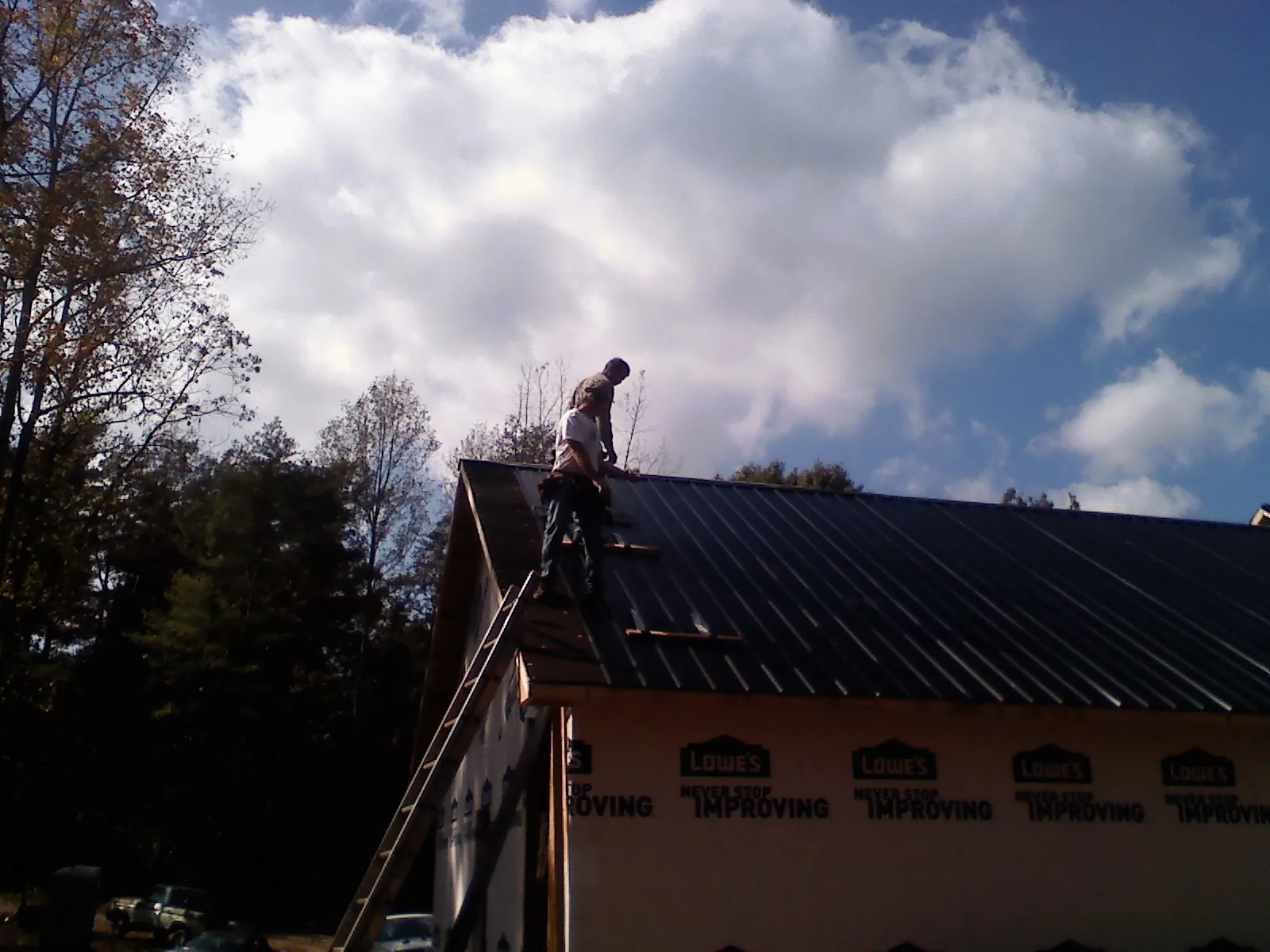 Roofer fastening dark metal panels high against a cloudy sky, from a Roof Inspection job in Pompton Plains