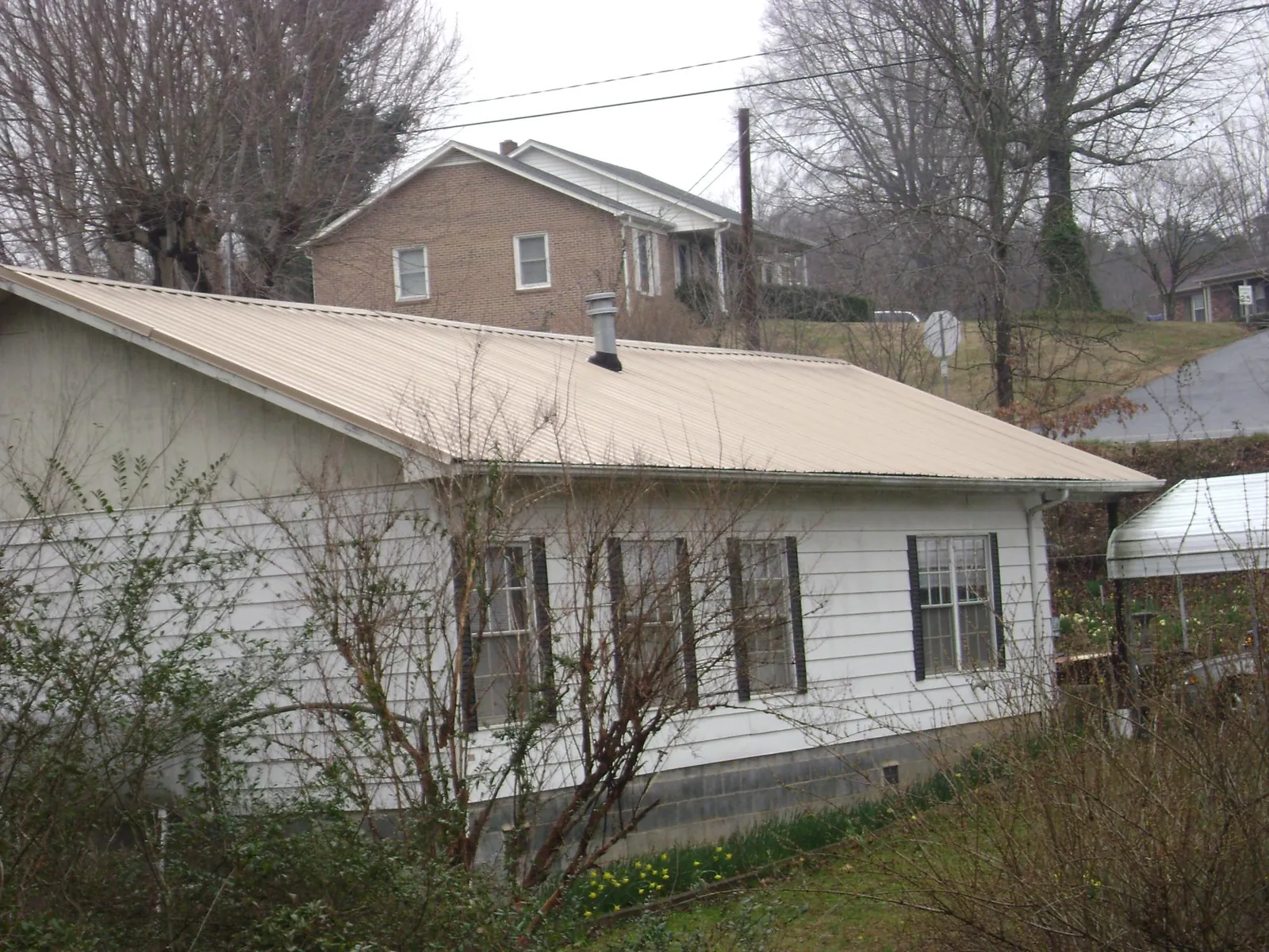 Tan metal roof on a white sided house set into a hillside — Commercial Roofing by Roofing Brothers in Pompton Plains